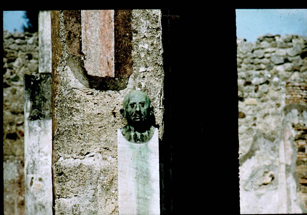 V.1.26 Pompeii. Room “b”, atrium. Reproduction bronze herm bust with wording - Genio L nostri Felix L.
(To the genius of our Lucius, Felix the freedman (erects)).
Photographed 1970-79 by Günther Einhorn, picture courtesy of his son Ralf Einhorn.

