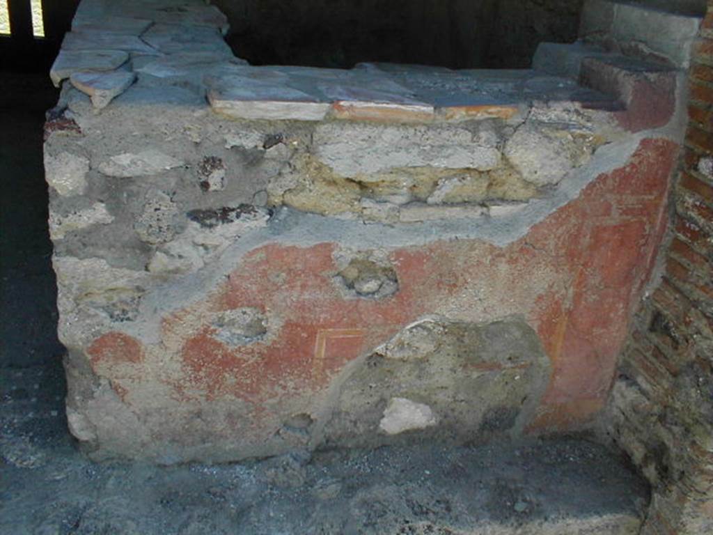 VI.16.33 Pompeii. May 2005. Remaining painted plaster on west-facing exterior side of counter. According to NdS, the outer surface of this counter had a red background. On the surface facing the road, according to Sogliano, obscene paintings were discovered. In the centre, in a yellow frame, was a large erect phallus. On each side, a male figure could be seen facing towards the centre panel and each other. The figure on the right was better preserved, and bald. There were also other painted panels and arabesques.See Notizie degli Scavi di Antichit, 1908, (p.289).
