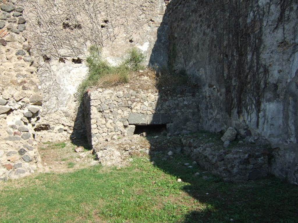 VII.12.7 Pompeii. September 2005. Looking east towards oven in south-east corner of rear area.
According to Boyce, on the south wall of the room with the oven was a large lararium painting (2.0 square).
In the centre was a blazing tripod, with the Genius to the right of it.
On each side was a wreathed Lar. 
To the left of this group stood Vesta, at her side was an ass with a bell around its neck.
On the right of the group stood Mercury.
In the lower zone, marked off from the upper by a brownish stripe, were the two serpents.
They were approaching a gold-coloured altar, on top of which was a white shallow dish containing a blazing fire.
In the fire was an egg and several fruits – a date, a pomegranate and a medlar.
See Boyce G. K., 1937. Corpus of the Lararia of Pompeii. Rome: MAAR 14. (p.70, no.313). 
See Helbig, W., 1868. Wandgemälde der vom Vesuv verschütteten Städte Campaniens. Leipzig: Breitkopf und Härtel. (68)
According to BdI, this was the first time that Mercury appeared associated with the Lares, in Pompeii.
See Bullettino dell’Instituto di Corrispondenza Archeologica (DAIR), 1864, p.114-115 (described as Casa II.)
