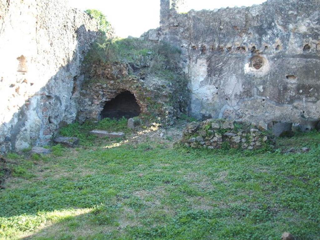 VII.12.13 Pompeii. December 2004. Lararium nNiche on east wall in front of oven in south east corner.   Two mills can be seen in the bakery area to the right of the oven.