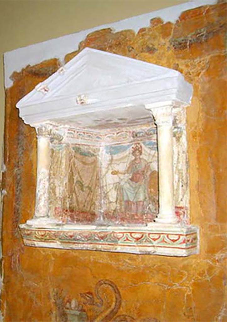 97. Gragnano, Villa rustica in Località Carmiano, Villa A. Lararium niche. 
From dividing pilaster between kitchen room 4 and room 2. 
Lararium in stucco found inserted in a yellow painted wall.
The lararium had a triangular pediment supported by two Corinthian columns.
The painting at the rear showed an enthroned Minerva with breastplate, helmet, shield, lance in the left hand and gilded/golden plate in the right. 
