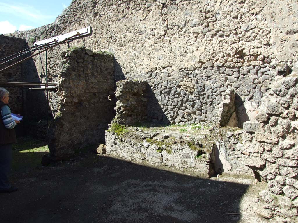 V.1.23 Pompeii. March 2009. Room “n”,  north wall of kitchen area, with bench. 
According to Boyce, in the kitchen on the wall at the side of the hearth was a lararium painting.  
In the middle was an altar around which a serpent was coiling and on the right of it stood the Genius.
On the left stood a Lar, the second Lar stood behind the Genius. 
Underneath there were another two serpents, further on the right side the figure of river Sarnus reclined, crowned with reeds and with a jar at his elbow. 
The background was filled with plants.
See Boyce G. K., 1937. Corpus of the Lararia of Pompeii. Rome: MAAR 14. (p.32, no.79) 
Nothing remains of the painted Lararium today.
Sogliano described the lararium and placed it at V.1.10, the kitchen at the rear entrance doorway.
In 1879, when his book was published, he described the lararium as a “representation of the Lares with Genius now destroyed, the plaster has fallen, and only the Sarnus figure remains sitting and crowned…..”.
See Sogliano, A., 1879. Le pitture murali campane scoverte negli anni 1867-79. Napoli: (p.15, no.37)
Sogliano quotes Bull.Inst.1876, p.246.

