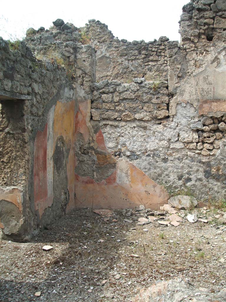 V.2.d Pompeii. May 2005. Room “c” the ala on north side of atrium, with doorway to cubiculum “e”, on left.
The low zoccolo was yellow, the middle zone of the walls was painted with red and yellow panels edged with “carpet” borders and two parallel lines.
These panels were separated by narrow white compartments containing a painted twisted candelabra design.
The north wall of the ala contained a large blocked-up window, which originally would have opened onto the long corridor of the neighbouring house at V.2.e.
