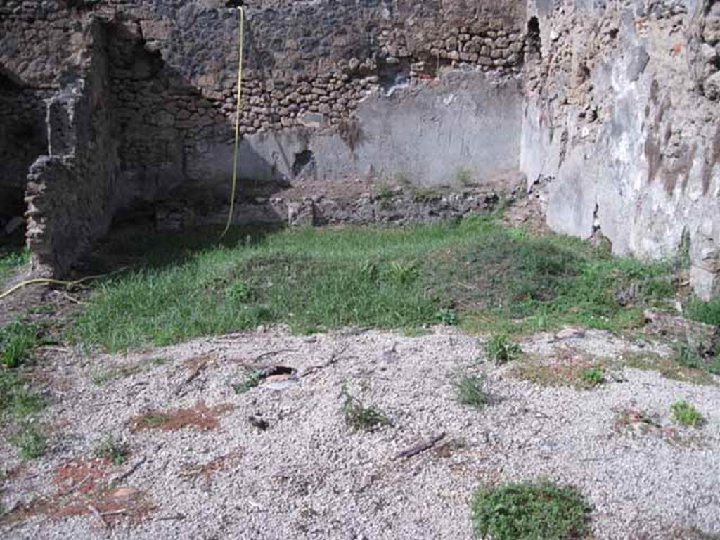 I.2.24 Pompeii. September 2010. 
Looking north across site of summer triclinium and peristyle, from south portico. Photo courtesy of Drew Baker.
According to Jashemski, this Caupona or Officina Libraria had a portico on the south and east sides of the garden area.
The columns were connected by a low wall with an entrance to the garden on the west.
The caupona was excavated in 1873. There was a masonry triclinium with a table in the garden.
Two large breaks in the triclinium, which is today badly damaged, reveal the amphorae used in its construction.
Fiorelli believed that the low podium along the north wall held pots of flowers.
Mau reported a drainage channel at the corner of the triclinium, but it is no longer visible.
Only the base of an aedicula lararium built against the east wall opposite the north end of the east couch can still be seen.
See Jashemski, W. F., 1993. The Gardens of Pompeii, Volume II: Appendices. New York: Caratzas. (p.25)

According to Boyce, in the east wall of the peristyle, above one of the beds of a masonry triclinium was a niche.
It was described by Fiorelli as a sacrario.
More fully described by Mau as an “aedicula, una base, con una piccola tavola, che sta in una specie di nicchia coperta a volta, e probabilmente conteneva un’idolo”.
There remains now only the solid base, (0.40 by 0.32, h.0.65) and on the wall above it, the marks left by a vaulted structure which rested on the base.
Bull. Inst, 1874, 262; Fiorelli, Descr., 47.
See Boyce G. K., 1937. Corpus of the Lararia of Pompeii. Rome: MAAR 14. (p.23, no.17) 
As this book was written in the 1930s, it is probable that there is now even less evidence of the niche, following the bombing in the near vicinity in 1943, and the damage of the 1980 earthquake.
Possibly the solid base may be visible on the extreme right of the above photo, but would need a clearer photo.
If the white lapilli is covering the site of the triclinium, then the stone in the photo would seem to be in the correct place, “against the east wall opposite the north end of the east couch”, but according to Boyce’s measurements appears to look too small.


