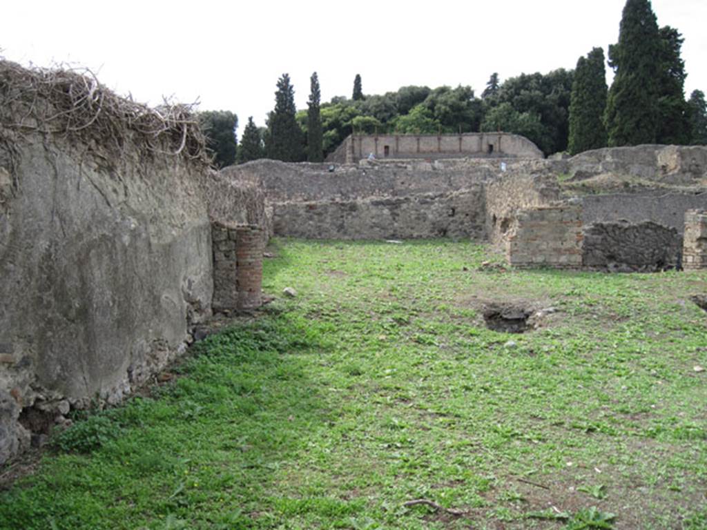 I.3.3 Pompeii. September 2010. Upper peristyle area, looking west towards the large exedra or triclinium, from the south-east corner. Photo courtesy of Drew Baker.
According to Warscher this was triclinium n, south-west of the peristyle. She wrote 
Nel pavimento cio si vede un ornamento di forma quadrata, formato di pietruzze bianche, che non stando nel bel mezzo, ma pi nellinterno della camera non poteva servir ad altra se non a segnar il posto ove fra letti si metteva la tavola.
Qui per non stavano che due letti, i cui posti bene si riconoscono dal pavimento meno consumato. Nel muro N e verso S vi sono fori per lasciar scolare lacqua. Le pareti sono decorate in nero con ornamenti architettonici nel terzo stile di Pompei (Giorn.Sc II, p.452 segg). Il quadro che in parte distrutto vi si trova fu descritto da me e spiegato per Ippolito con la nutrice nel Bull. 1873, p.273. Poi seguiva verso N un corridoio obbliquo che dirigendosi verso latrium conduceva alle stanze superiori. Ma di questo corridoio nulla  rimasto: si riconosce soltante dalle buche de travi che lo sorreggevano (see photograph no.1, at I.3.1)
See Warscher, T, 1935: Codex Topographicus Pompejanus, Regio I, 3:  Rome, DAIR.  
(translation:  "In the floor one could see a square-shaped ornament that was formed from white stones, that were not in the beautiful middle, but more in the inside of the room where they could only serve as a sign to show the place where one put the table, between the couches. Here, however, there were only two beds, their place known well from the floor less worn.  In the north wall and towards the south, there were holes to let the water drain. The walls were decorated in black with architectural ornaments in the Third Style of Pompeii (Giorn.Sc II, p.452 following). The picture found here that was partly destroyed, was described by me and explained as Hippolytus with the nurse, in Bull. 1873, p. 273. Then followed towards the north, a sloping corridor that pointed towards the atrium leading to the upper rooms. But nothing remained of this corridor: one can recognize only the holes of the beams that supported it ... " (see photograph no.1, at I.3.1).

