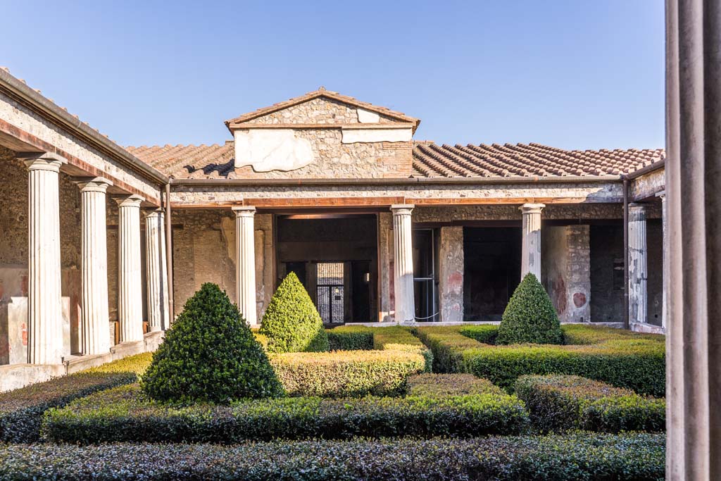 I.10.4 Pompeii. April 2022. 
Looking north across peristyle garden from south-west portico. The doorway to room 11 is behind the columns, on the left.
Photo courtesy of Johannes Eber.

