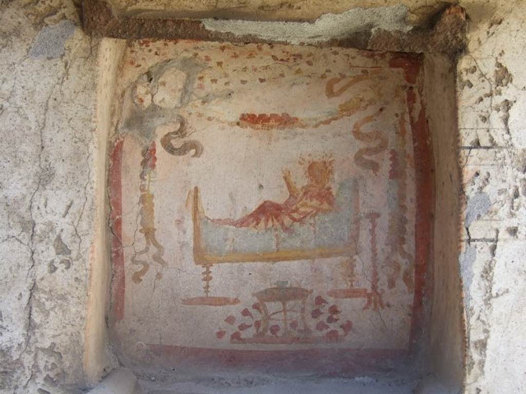 I.14.7 Pompeii. March 2009. West wall of garden area.  
Niche lararium with painting of a god in a long white robe lying on a couch.  
The right hand holds a branch and the left holds a patera.  
To the right is a golden candelabrum.  
At the front is a three legged table with a bowl of fruit.  Above is a garland.
See Frhlich, T., 1991. Lararien und Fassadenbilder in den Vesuvstdten. Mainz: von Zabern. (L34, T:29,3)
