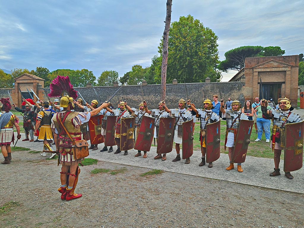 II.7.5 Pompeii, on right. September 2024. 
Looking west on Piazzale Anfiteatro towards legionaries with swords raised and the Palaestra during “Ludi Pompeiani” event. Photo courtesy of Giuseppe Ciaramella.

