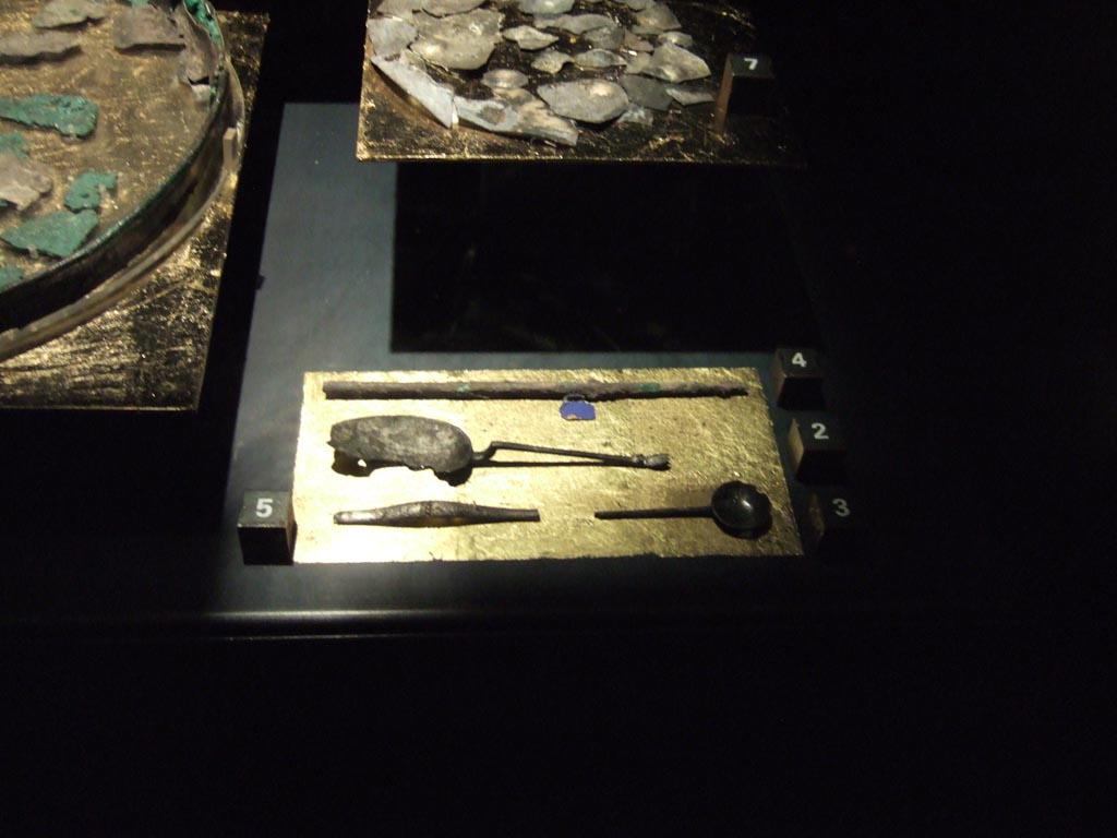 Four silver items found 20th September 1887 in VIII.2.23. Now in Naples Archaeological Museum.
Fragment of a wine tube (top). Inventory number 116360.
Oval spoon with raised handle (centre). Inventory number 116357.
Fragment of a long handle probably of a simpulum (bottom left). Inventory number 116362. 
Round spoon (bottom right). Inventory number 116358.
See Guzzo, P. (A cura di), 2006. Argenti a Pompei. Milano, Electa. (p. 134).
