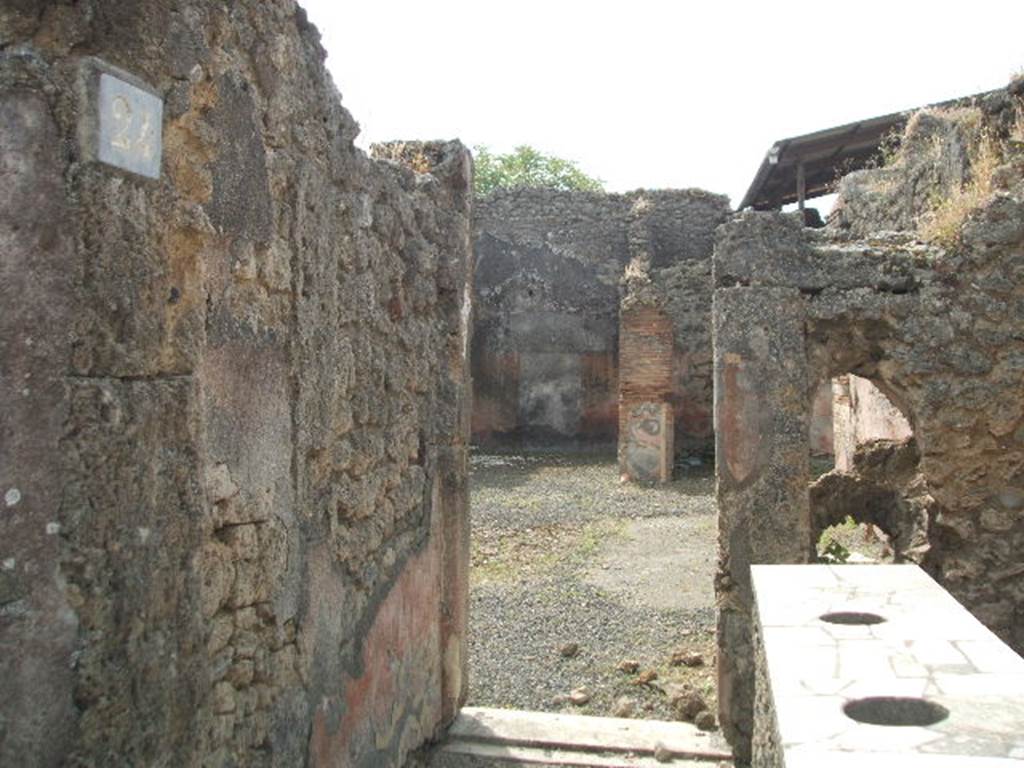 IX.7.24 Pompeii. May 2005. Looking south across thermopolium (a) to doorway to atrium (2) of IX.7.25
The doorway between the shop and the atrium had the threshold of a dark marble and was closed by two battens.  
See Mau in Bullettino dell’Instituto di Corrispondenza Archeologica (DAIR), 1882, (p.148)
According to Boyce, in the south wall was a vaulted niche (h.0.44, w.0.44, d.0.51, h. above floor 1.20).
Its inside walls were coated with orange-coloured stucco.
Above the niche was a painting (h.0.30, w.0.73) of the two serpents confronting at an altar.
He references – Not. Scavi, 1880, 395; Bull. Inst., 1882, 148.
See Boyce G. K., 1937. Corpus of the Lararia of Pompeii. Rome: MAAR 14. (p.88 no.443). 

