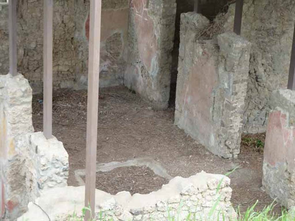 IX.14.c Pompeii. May 2010. Looking north across atrium 2 with impluvium (a), which was square consisted of a simple groove in the floor. At the north end of the impluvium was a masonry feature, yellow on the outside, semi-circular inside. There was a hole in the centre from which water flowed into the impluvium. The atrium floor and that of the fauces were of opus signinum. On the west side of the Tuscan atrium was a cistern mouth (b) made of lava stone. There are two doors in rear (east) wall. The narrower doorway is the entrance to room 6. The wider (nearer) doorway is to the small portico 9 and this leads to the garden 3 and kitchen and latrine 11.
