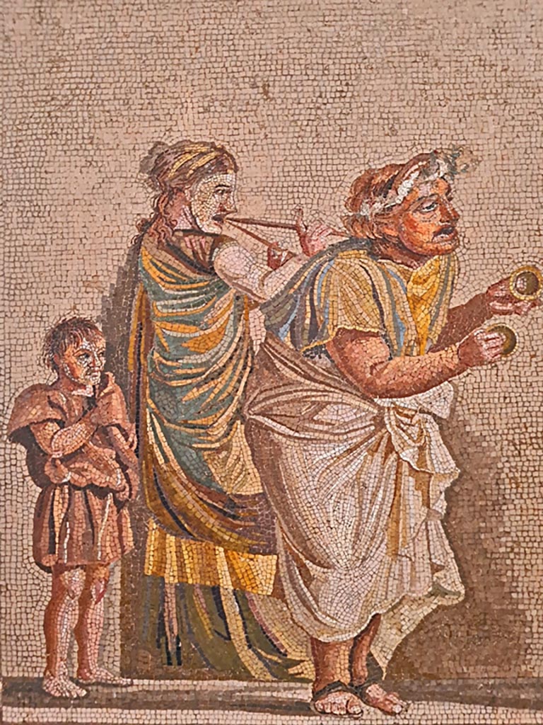 HGW06 Pompeii. Found on 8th April 1763. Ambiente 13 of Villa of Cicero. 
Detail from mosaic of a Group of Street Musicians – 
a musician playing cymbals on the right, in the centre a woman with a double flute, and on the left, a boy follows the procession.
Now in Naples Archaeological Museum. Inventory number 9985.
Photo courtesy of Giuseppe Ciaramella. September 2024.
